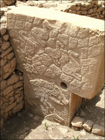 Image of Göbekli Tepe pillar showing detailed relief carvings as well as  
				abutting secondary surrounding walls